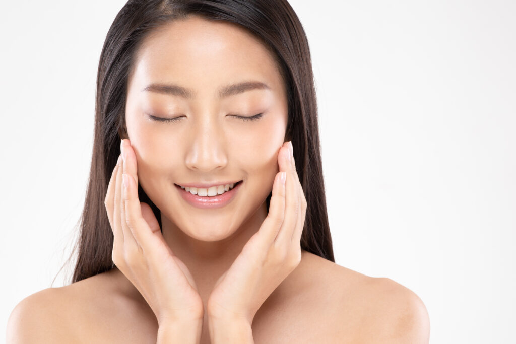 Beautiful Asian young woman smiling and touching her cheeks with her hands with her eyes closed.